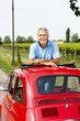 Mature man enjoying a road trip in a small red car