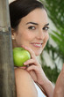 a brunette woman with an apple leaning against a bamboo stick