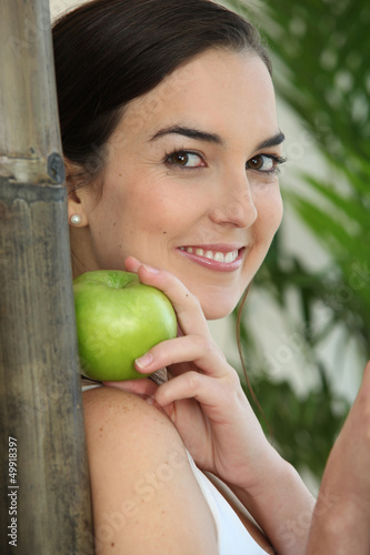 Photo: a brunette woman with an apple leaning against a bamboo stick a brunette woman with an apple leaning against a bamboo stick