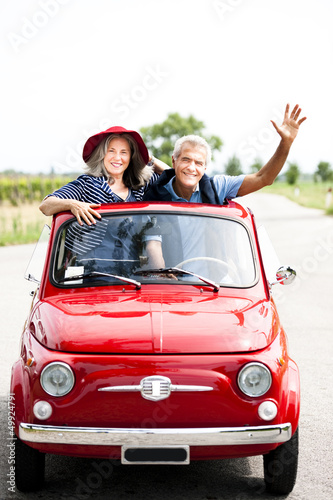 Photo: Mature couple enjoying a road trip in a small red car Mature couple enjoying a road trip in a small red car