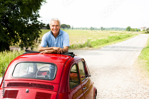Photo: Mature man enjoying a road trip in a small red car Mature man enjoying a road trip in a small red car