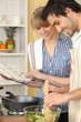 Woman and man smiling cooking using cookbook