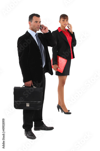 Photo: businessman and businesswoman talking on their cells businessman and businesswoman talking on their cells