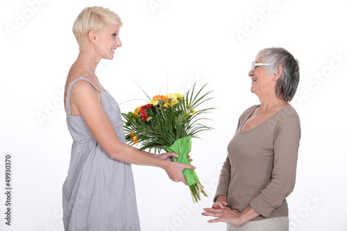 Photo: Young woman offering a bouquet of flowers to her grandmother Young woman offering a bouquet of flowers to her grandmother
