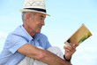 A mature man reading a book outside.