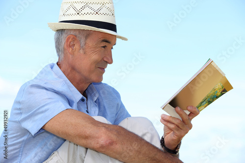 Photo: A mature man reading a book outside. A mature man reading a book outside.