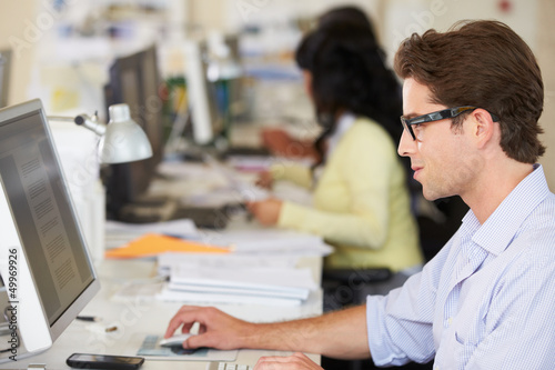 Photo: Man Working At Desk In Busy Creative Office Man Working At Desk In Busy Creative Office