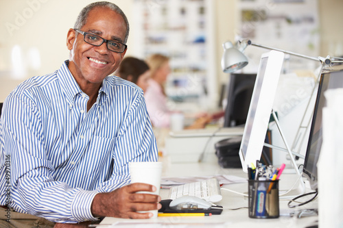 Photo: Man Holding Cup Working At Desk In Busy Creative Office Man Holding Cup Working At Desk In Busy Creative Office