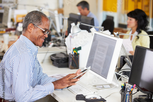 Photo: Man Using Digital Tablet In Busy Creative Office Man Using Digital Tablet In Busy Creative Office