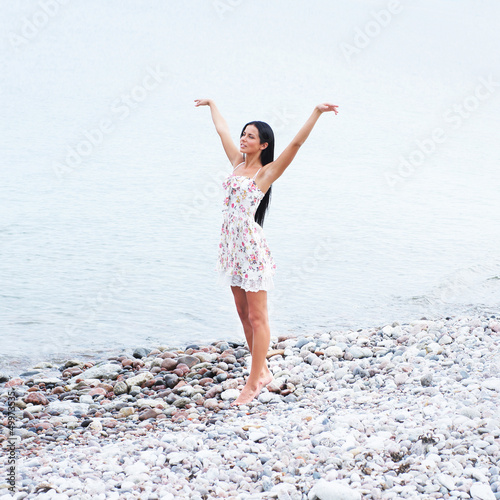 Photo: A young woman in a summer dress on a blue sea background A young woman in a summer dress on a blue sea background