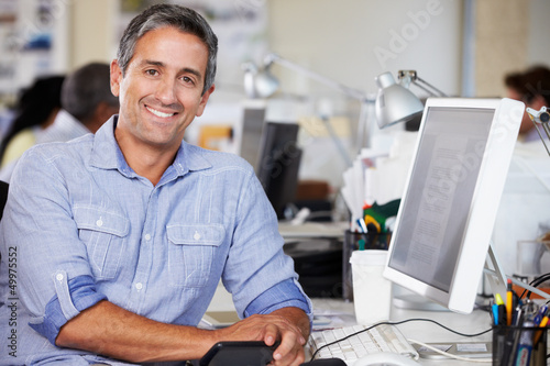 Photo: Man Working At Desk In Busy Creative Office Man Working At Desk In Busy Creative Office