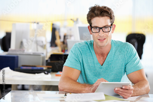 Photo: Man Using Digital Tablet In Busy Creative Office Man Using Digital Tablet In Busy Creative Office