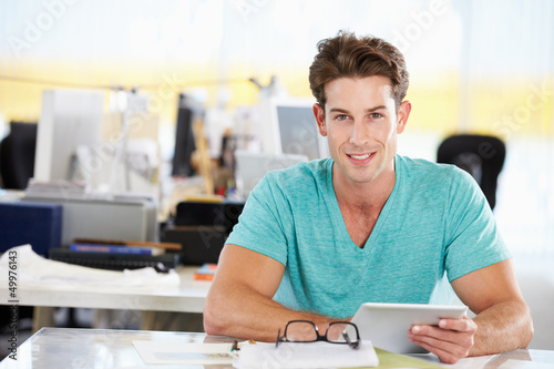 Photo: Man Using Digital Tablet In Busy Creative Office Man Using Digital Tablet In Busy Creative Office