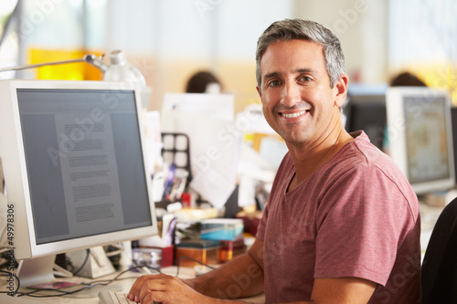 Photo: Man Working At Desk In Busy Creative Office Man Working At Desk In Busy Creative Office