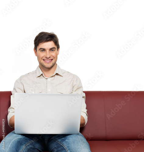 Photo: smiling happy man with laptop sits on the divan smiling happy man with laptop sits on the divan