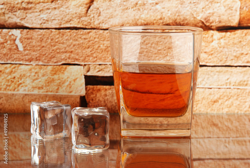 Photo: Glass of whiskey and ice on brick wall background Glass of whiskey and ice on brick wall background