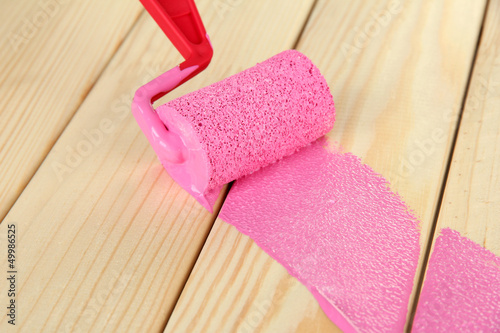 Photo: Paint roller brush with pink paint, on wooden background Paint roller brush with pink paint, on wooden background