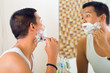 Asian man shaving in front of mirror