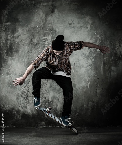 Photo: Young man in hat and shirt performing stunt on skateboard Young man in hat and shirt performing stunt on skateboard
