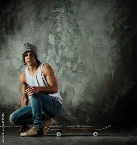 Photo: Young man in hat and jeans sitting near skateboard Young man in hat and jeans sitting near skateboard