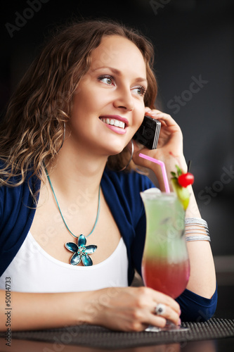 Photo: Happy young woman with cocktail calling on the phone Happy young woman with cocktail calling on the phone
