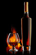 Bottle and glass with cognac over dark background with flame