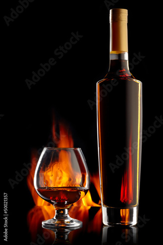 Photo: Bottle and glass with cognac over dark background with flame Bottle and glass with cognac over dark background with flame