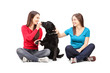 Two female friends sitting and playing with a dog