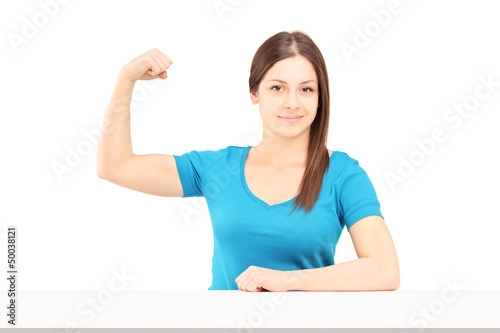 Photo: A young smiling woman showing her bicep muscle A young smiling woman showing her bicep muscle