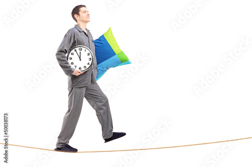 Photo: Full length portrait of a young man with pillow and clock sleepw Full length portrait of a young man with pillow and clock sleepw