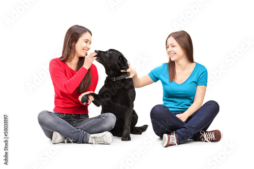 Photo: Two female friends sitting and playing with a dog Two female friends sitting and playing with a dog