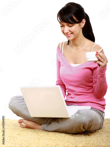 Photo: Young woman using laptop sitting on the floor and holding cup Young woman using laptop sitting on the floor and holding cup