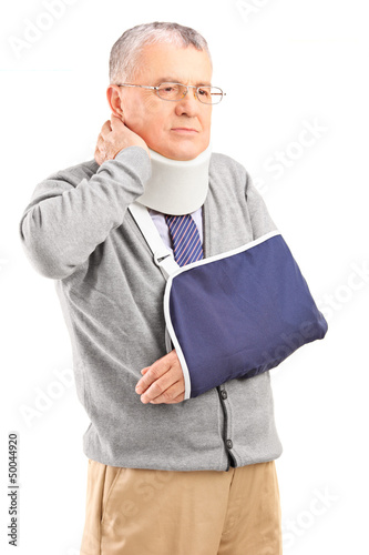 Photo: Senior man in pain wih a broken arm holding his neck Senior man in pain wih a broken arm holding his neck
