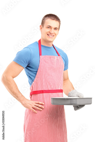 Photo: Smiling young man in an apron holding a baking tray Smiling young man in an apron holding a baking tray