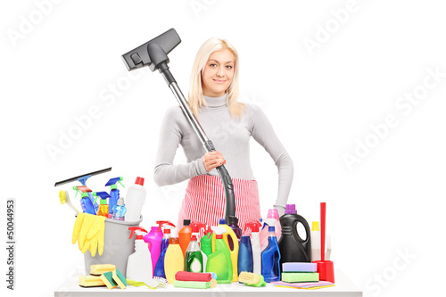Photo: Young smiling woman with a hover and cleaning supplies on a tabl Young smiling woman with a hover and cleaning supplies on a tabl