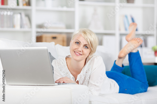 Photo: lächelnde frau liegt mit laptop auf dem sofa lächelnde frau liegt mit laptop auf dem sofa