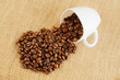 Roasted coffee beans with cup on jute hessian background