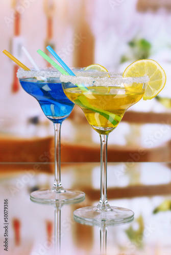 Photo: Yellow and blue cocktails in glasses on room background Yellow and blue cocktails in glasses on room background