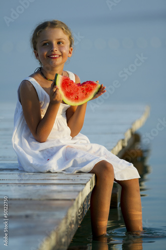Photo: Summer joy, girl eating fresh watermelon on the pier Summer joy, girl eating fresh watermelon on the pier