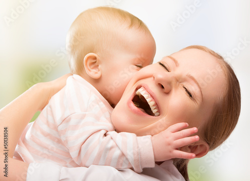 Photo: Happy cheerful family. Mother and baby kissing Happy cheerful family. Mother and baby kissing
