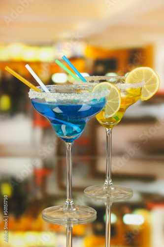 Photo: Yellow and blue cocktails in glasses on room background Yellow and blue cocktails in glasses on room background