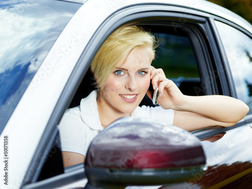 Photo: Blond girl sitting in her car has a call with smartphone Blond girl sitting in her car has a call with smartphone