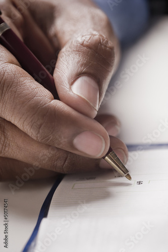 Photo: Mixed race man writing a check Mixed race man writing a check