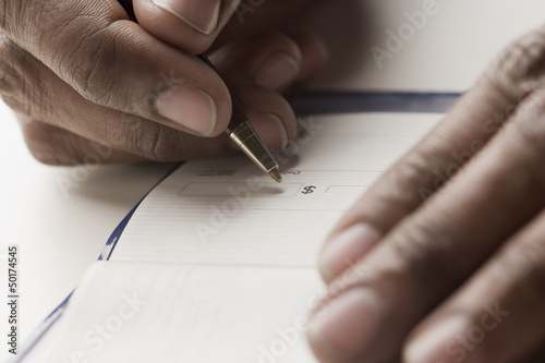 Photo: Mixed race man writing a check Mixed race man writing a check