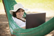 Happy woman working while resting in a hammock outdoors