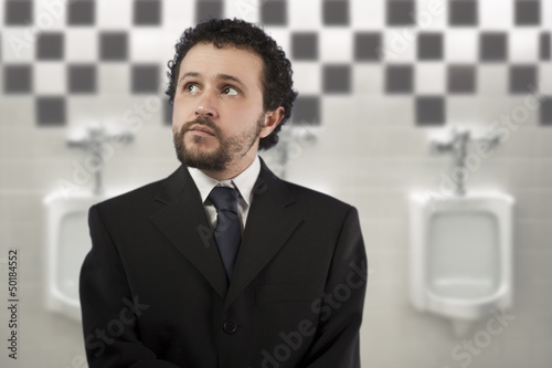 Photo: businessman with a distracted look urinating in urinals businessman with a distracted look urinating in urinals