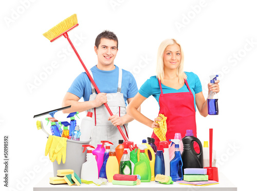 Photo: Male and female cleaners posing with cleaning supplies on a tabl Male and female cleaners posing with cleaning supplies on a tabl