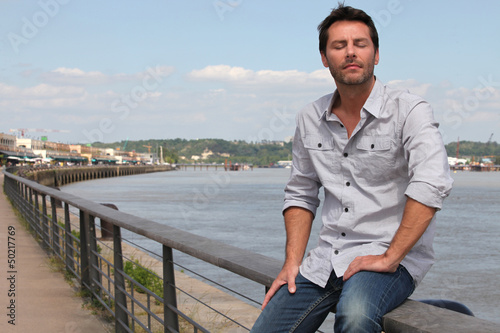 Photo: Man sitting by river. Man sitting by river.