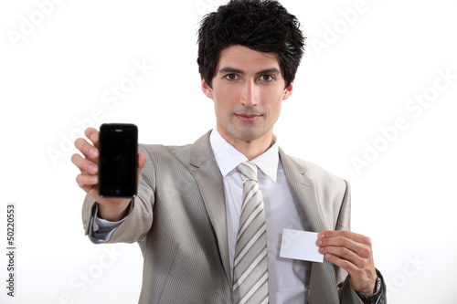 Photo: Businessman holding a blank business card and his phone Businessman holding a blank business card and his phone