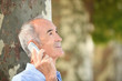 Grey-haired man with mobile telephone stood by tree